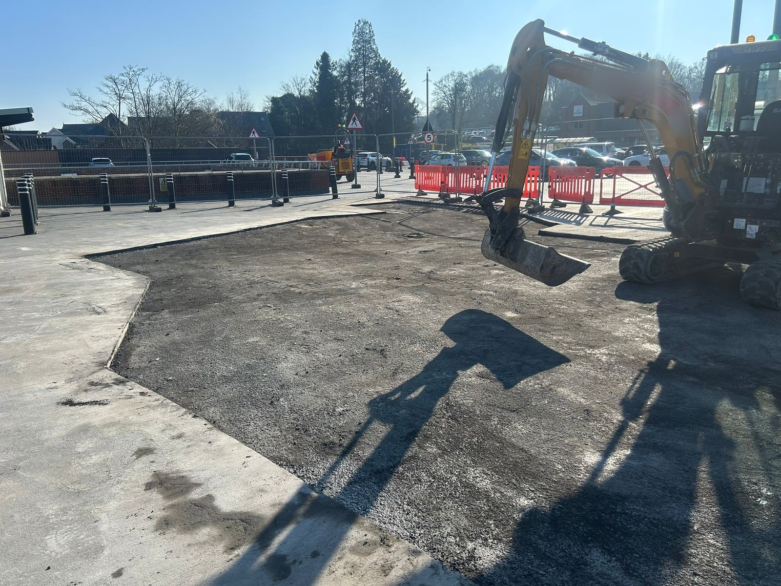 Mini excavator on a car park resurfacing job, with the new base laid behind barriers