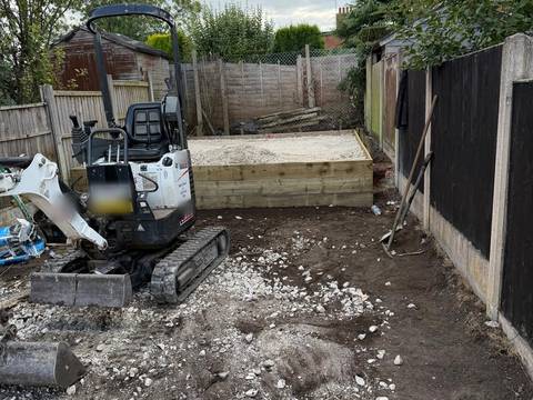 Micro digger in a cleared back garden beside a timber sleeper base filled with gravel