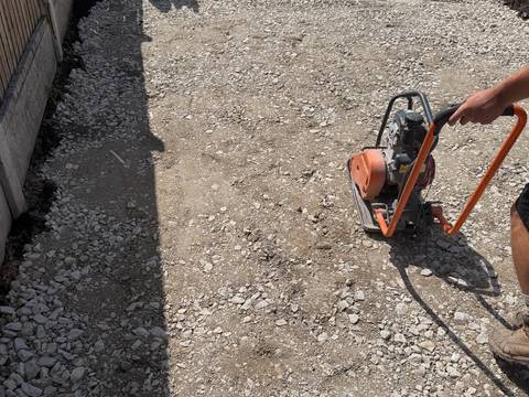 Plate compactor on a crushed-stone sub-base along a garden fence line