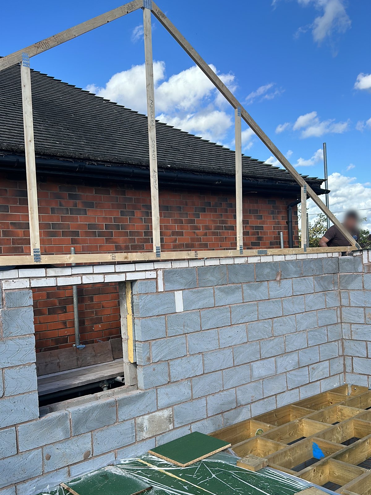 Timber roof frame going up on a single-storey extension, with floor joists and boards in place